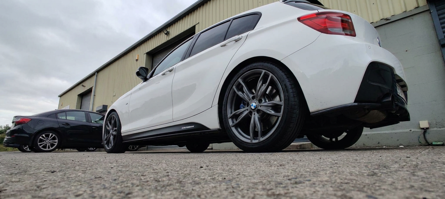 Low angle rear three-quarter of a white BMW 1 Series showing the tinted rear quarter glass