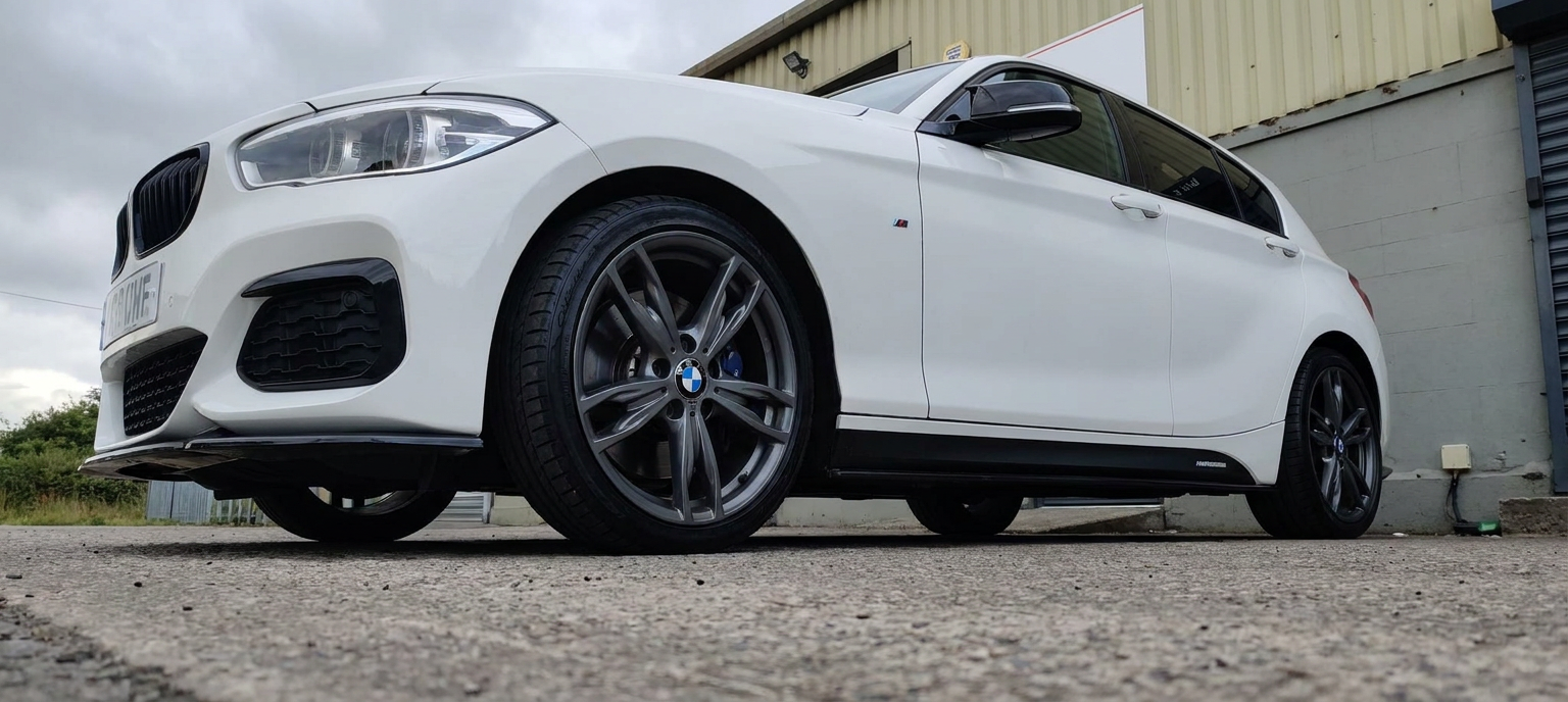 Low angle front three-quarter of a white BMW M140i with tinted side glass