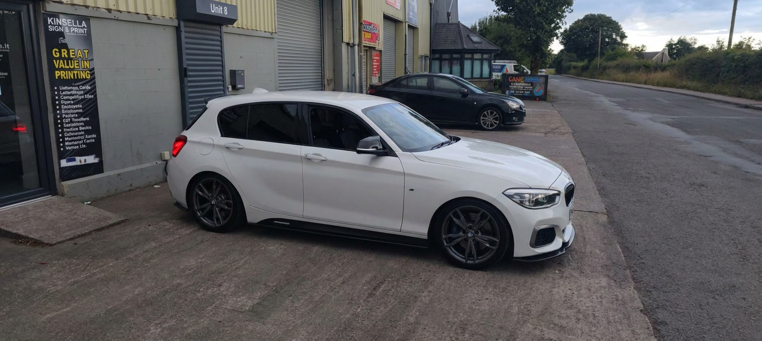 Front-right side profile of a white BMW M140i showing dark rear door tint
