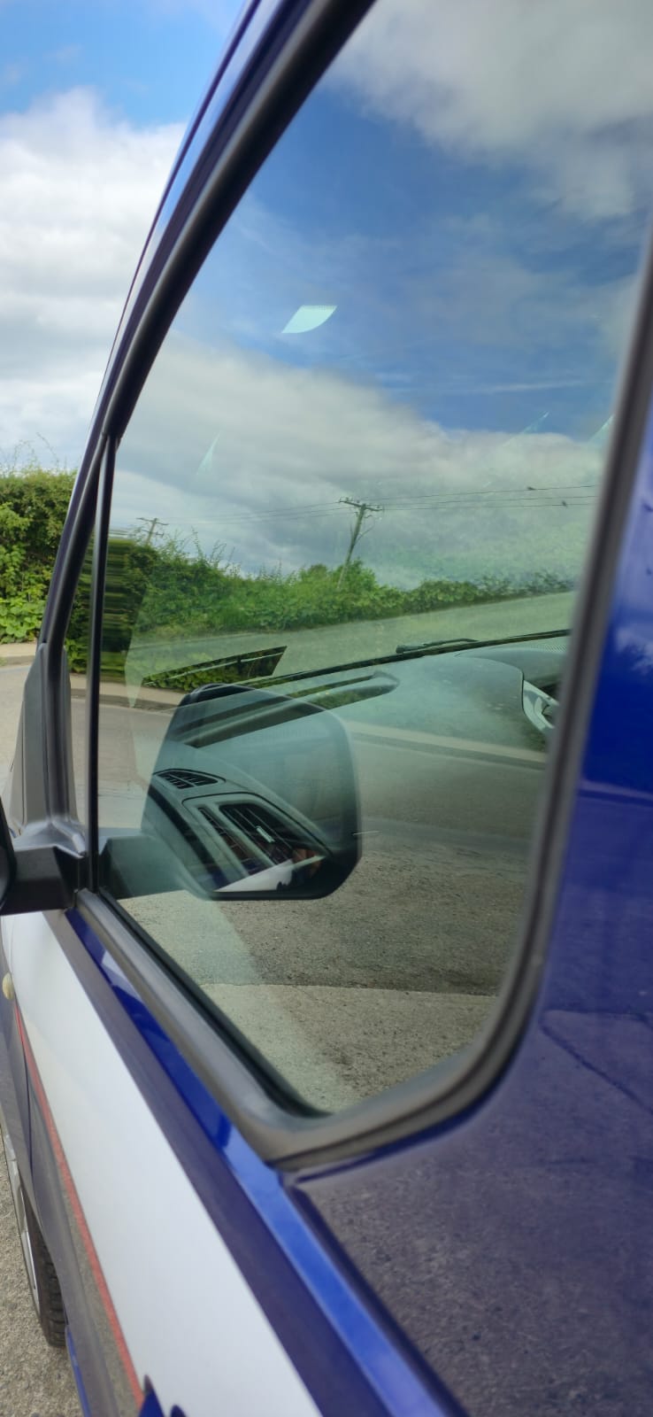 Blue van front side window with a clean heat-shrunk tint edge along the seal